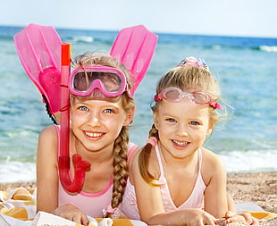 two girls wearing pink bikini behind seashore during daytime